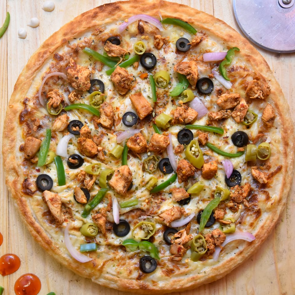 A PieZanos chicken pizza with green peppers, onions, and black olives on a wooden surface.