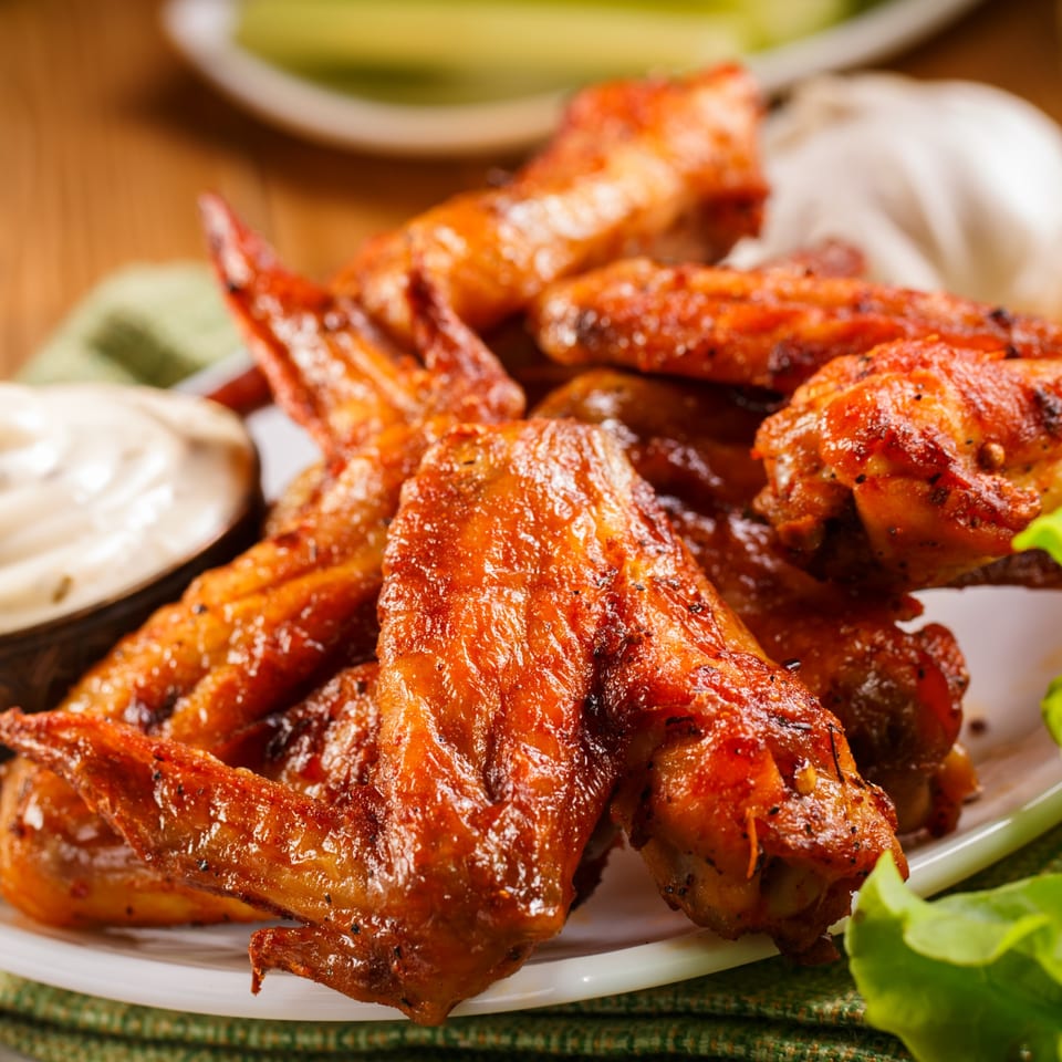 Close-up of crispy, golden-brown chicken wings with a side of dipping sauce and fresh lettuce.