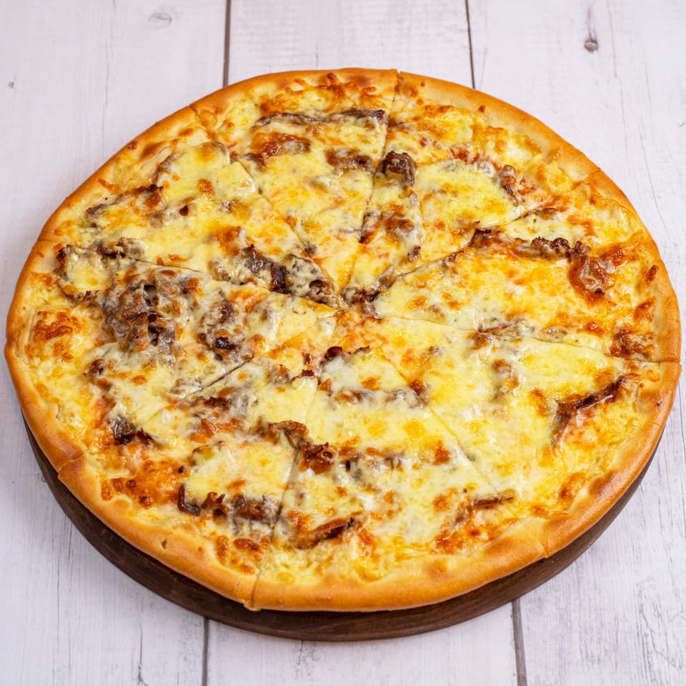A whole PieZanos pizza, cut into slices, with melted cheese and meat toppings on a wooden board.