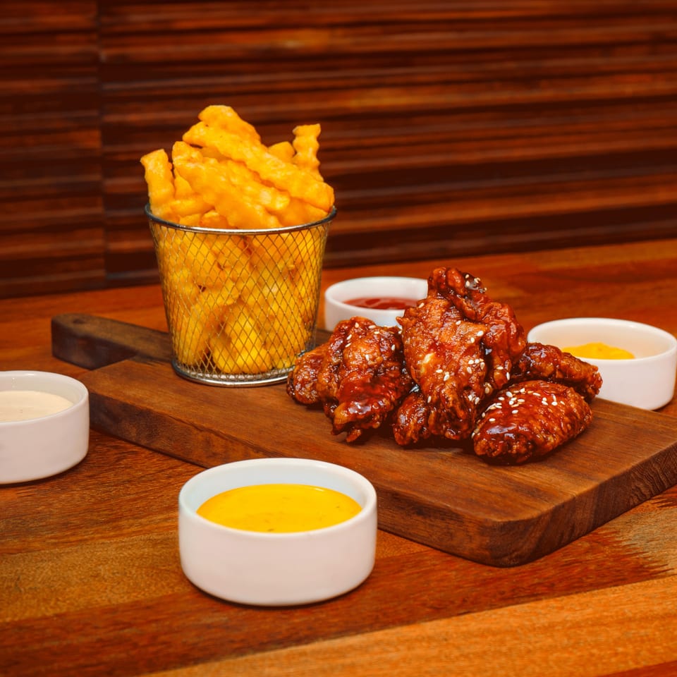 Crispy PieZanos wings with sesame seeds, a basket of fries, and dipping sauces on a wooden board.